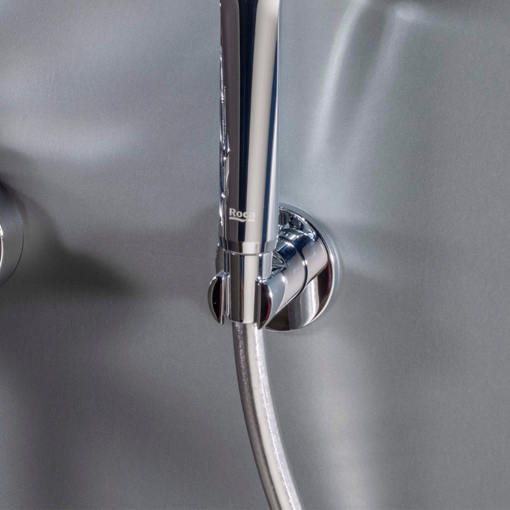 Lifestyle image of the Roca Round Chrome Shower Handset Bracket mounted on a wall and holding a handset shower